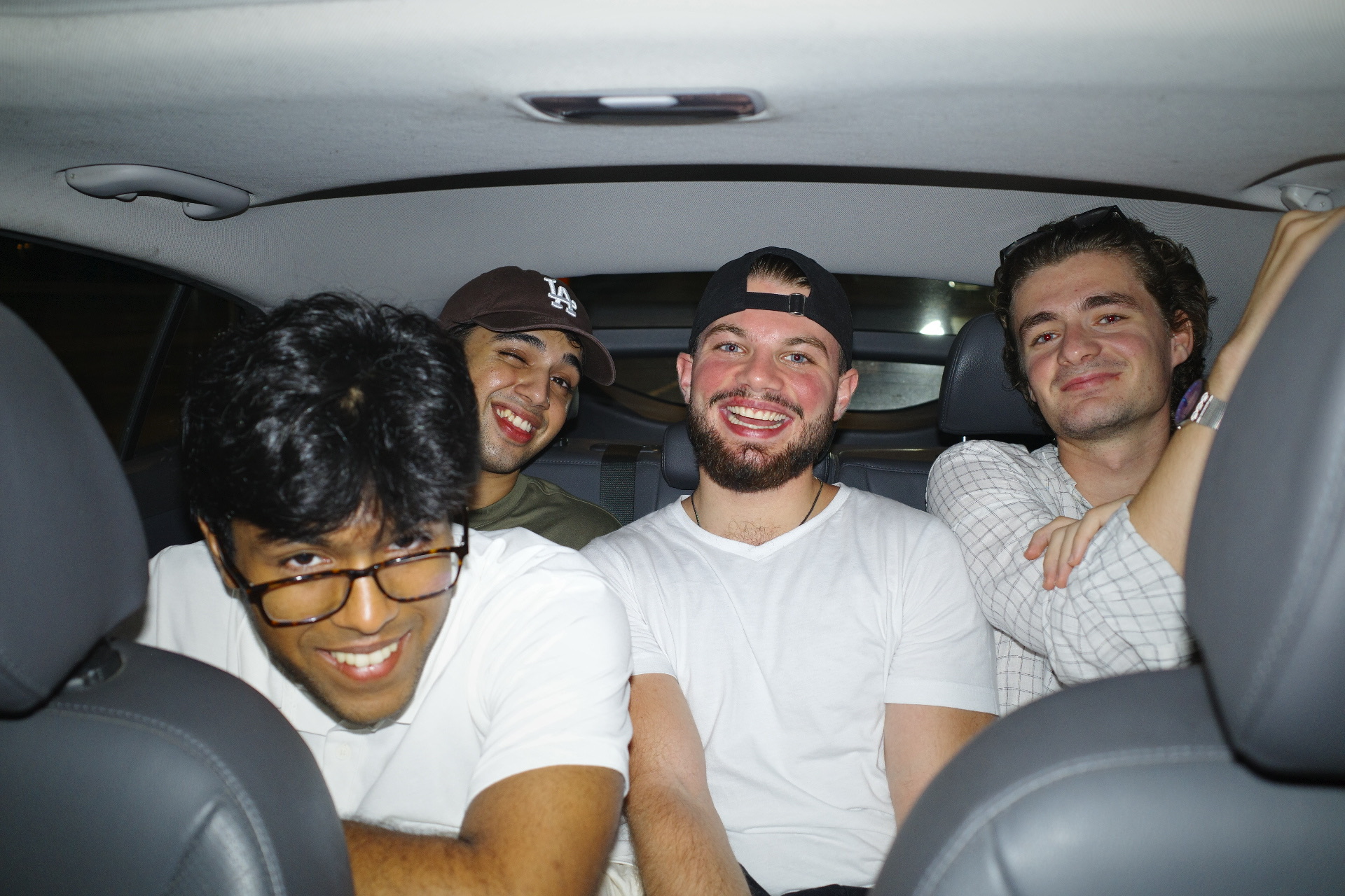Four friends squeezed into the back seat of a car, laughing