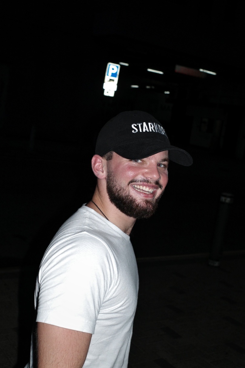 The founder laughing in a white t-shirt and black STARKBRO cap, shot on flash at night