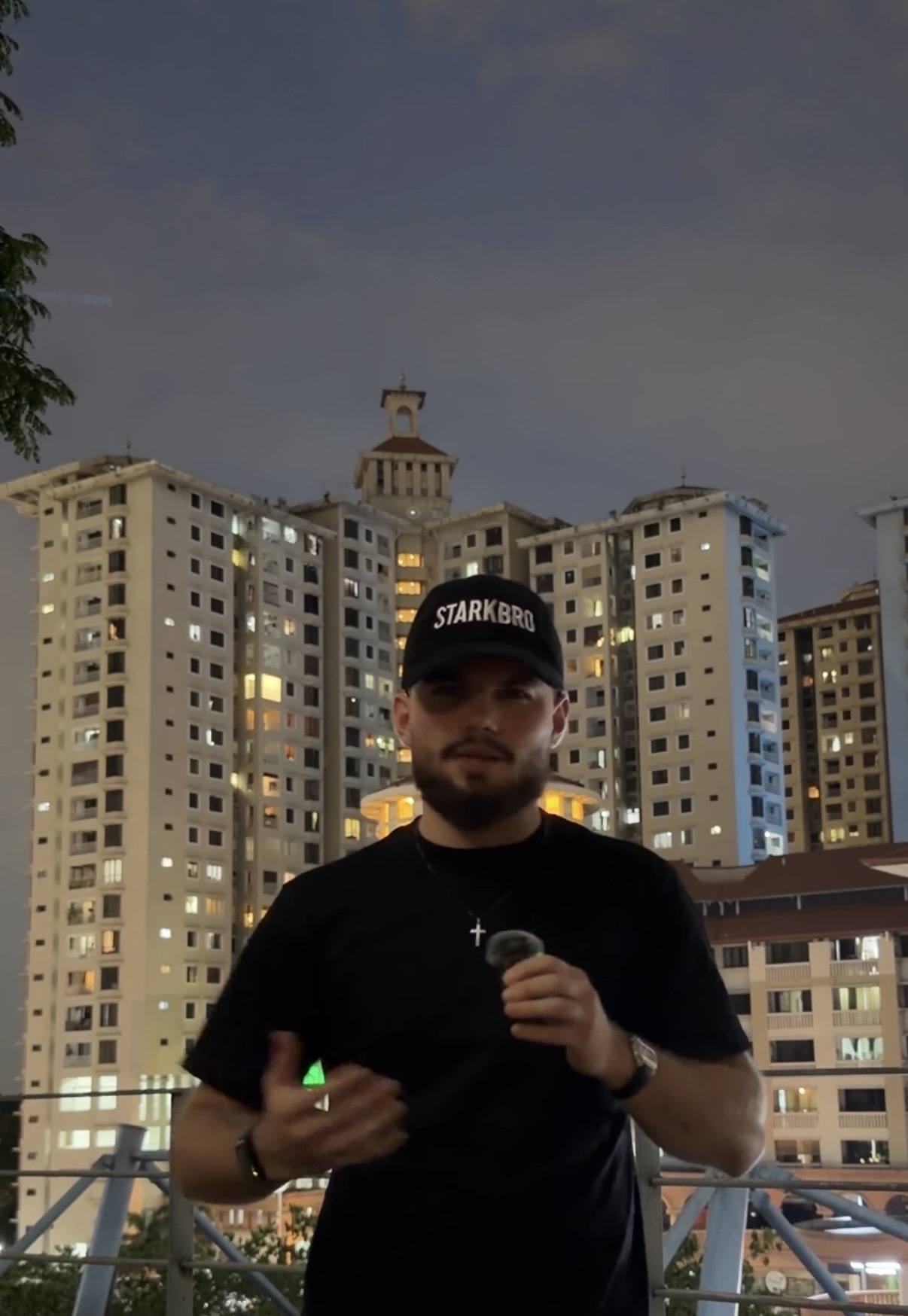 The founder wearing a black STARKBRO cap at night in front of illuminated apartment towers